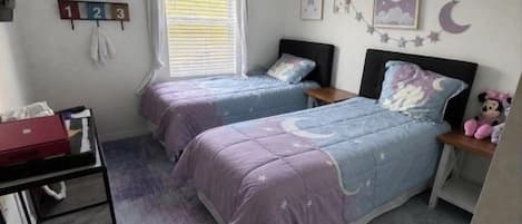 Ein Schlafzimmer mit zwei Betten, einem Deckenventilator, einem Fenster mit Jalousien und einer Wanduhr.