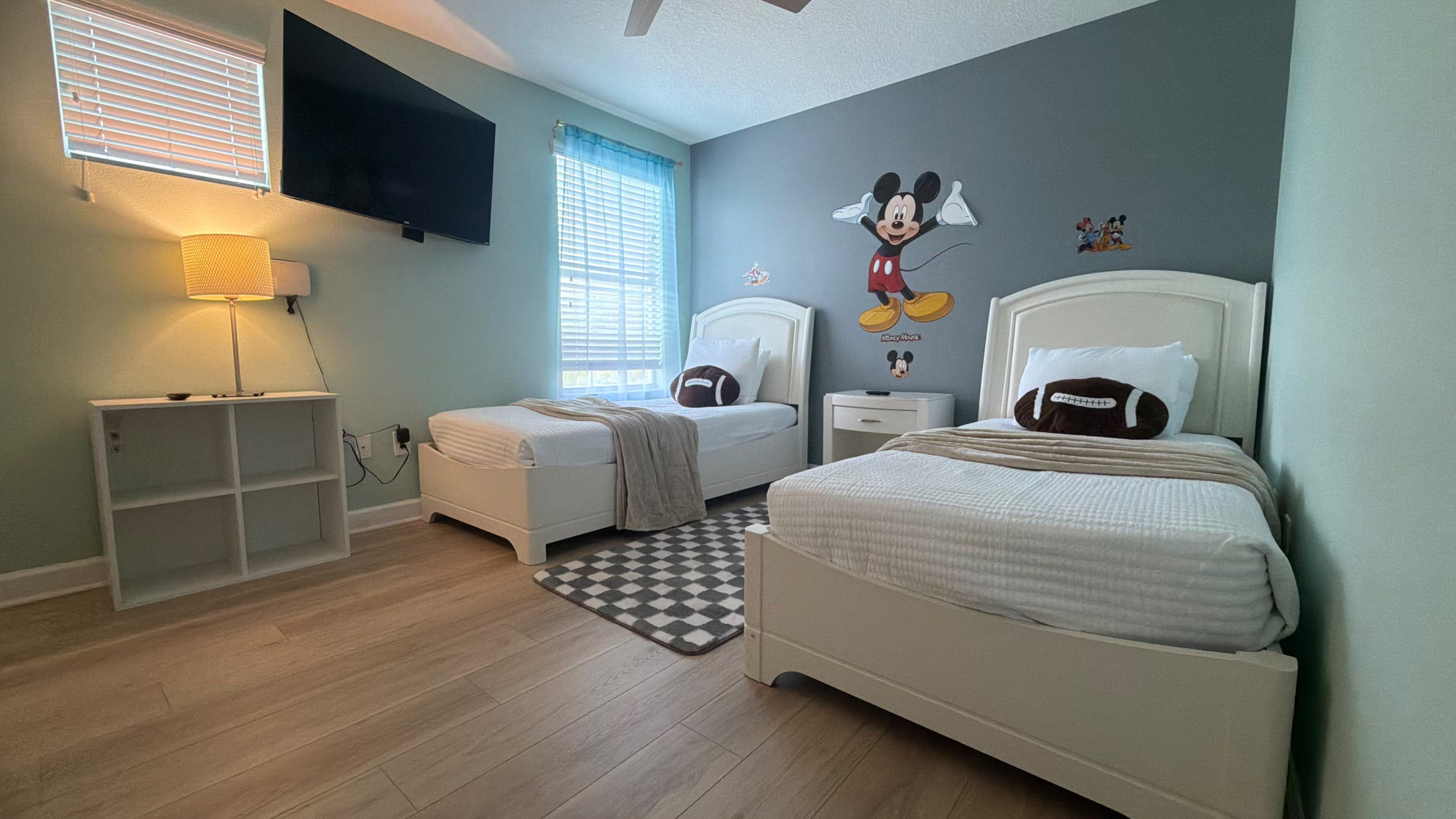 A bedroom with two beds, a TV, a lamp, and Mickey Mouse wall decals.