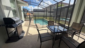 Eine Terrasse im Freien mit Grill, Sitzgelegenheiten und Blick auf einen Swimmingpool.