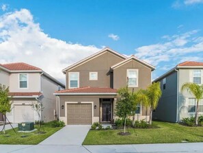 A residential building with a central garage, a front lawn, and a clear sky. - Elegant 5 BD/ 5 BA/ Paradise Palms - 9004 MP (Kissimmee)