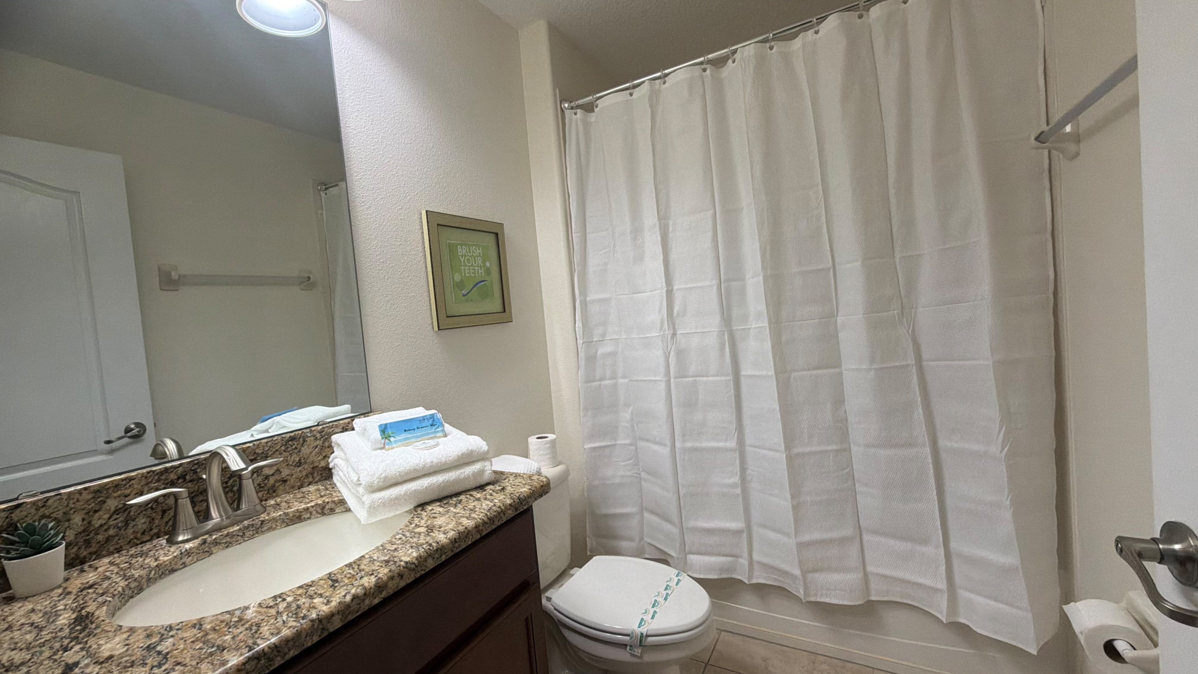 A bathroom with a granite countertop sink, a white toilet, and a shower curtain.