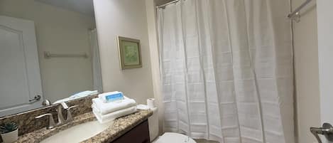A bathroom with a granite countertop sink, a white toilet, and a shower curtain.