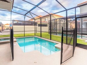 A swimming pool with a glass enclosure, surrounded by a paved area. - Elegant 5 BD/ 5 BA/ Paradise Palms - 9004 MP (Kissimmee)