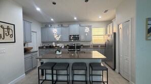A modern kitchen with a central island, bar stools, stainless steel appliances, and pendant lighting. - Elegant 5 BD/ 5 BA/ Paradise Palms - 9004 MP (Kissimmee)