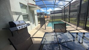 An outdoor patio with a grill, a glass table, and a pool. - Elegant 5 BD/ 5 BA/ Paradise Palms - 9004 MP (Kissimmee)