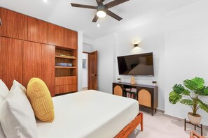 Ein Schlafzimmer mit einem Bett, einem Holzschrank, einem Fernseher und einer Topfpflanze.