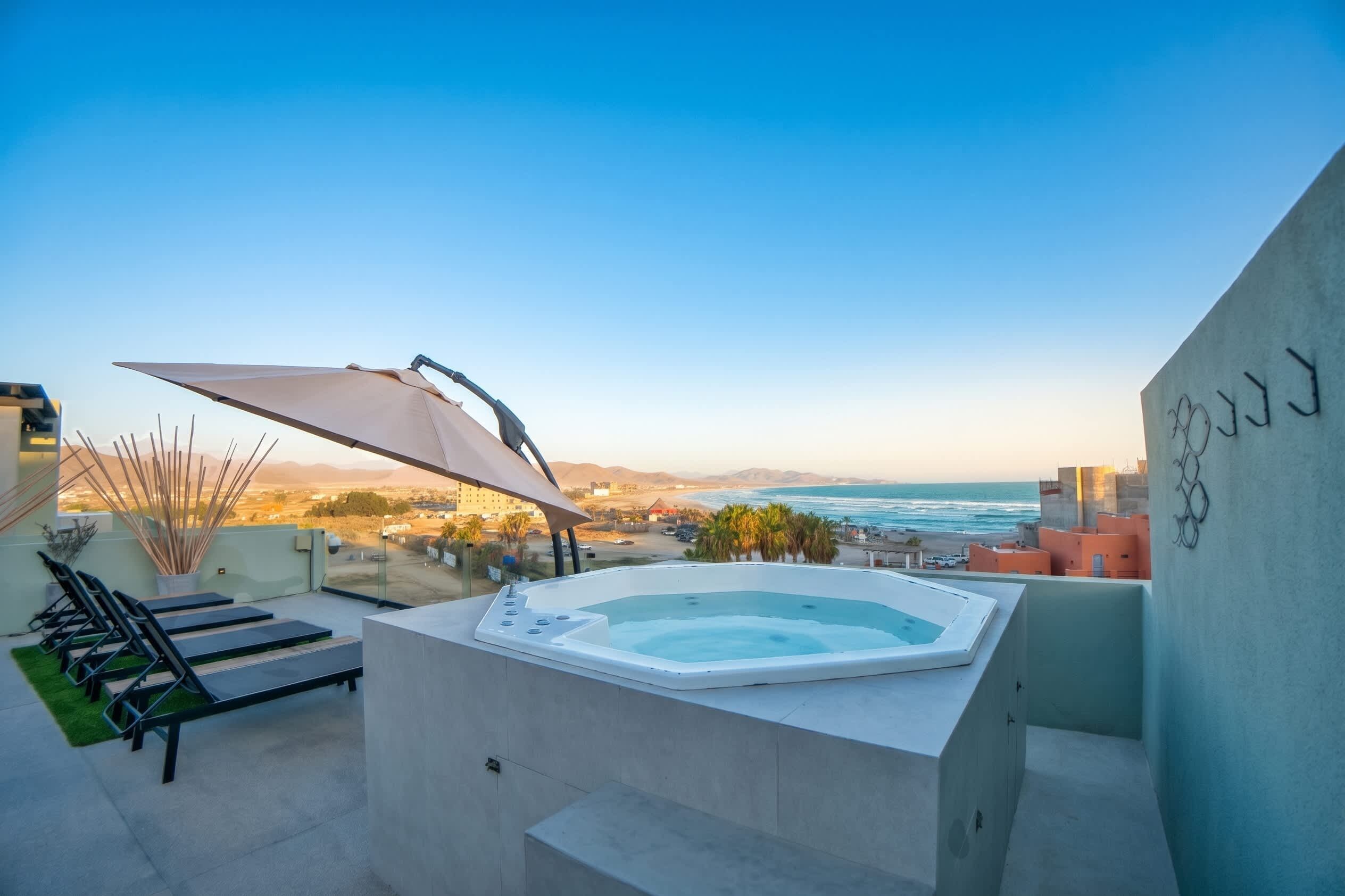 A rooftop terrace with a hot tub, lounge chairs, and a view of the ocean.