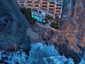 Eine Luftaufnahme eines Küstenhotels mit mehreren Gebäuden, einem Swimmingpool und einer felsigen Küstenlinie.
