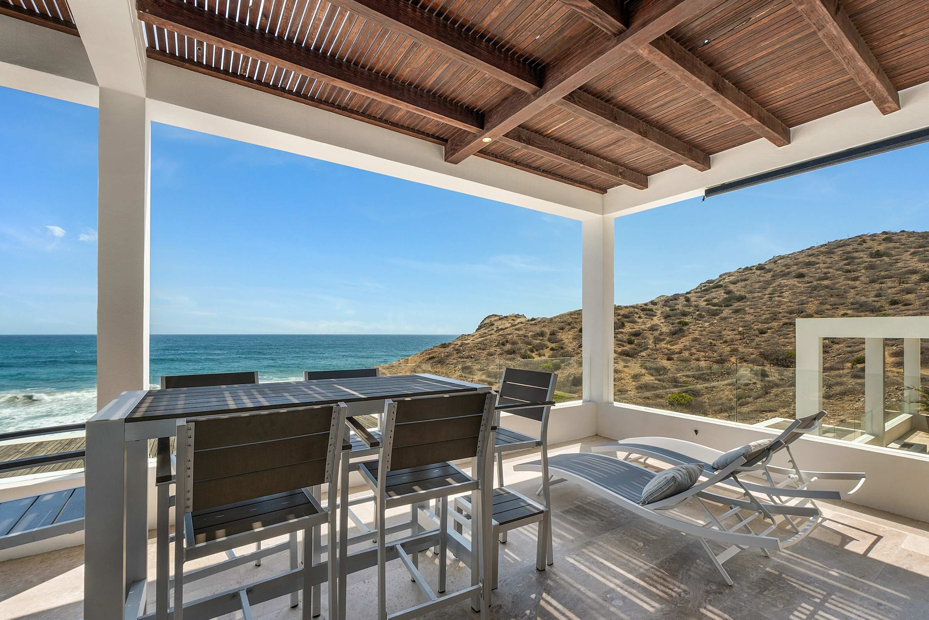 A covered outdoor seating area with a view of the ocean and hills.