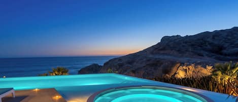 Una piscina amb un banyera d'hidromassatge, amb vista a una costa rocosa a la posta de sol.