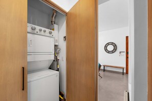 Une buanderie équipée de machines à laver et de sèche-linge superposés, d’un banc et d’un grand miroir rond fixé au mur.