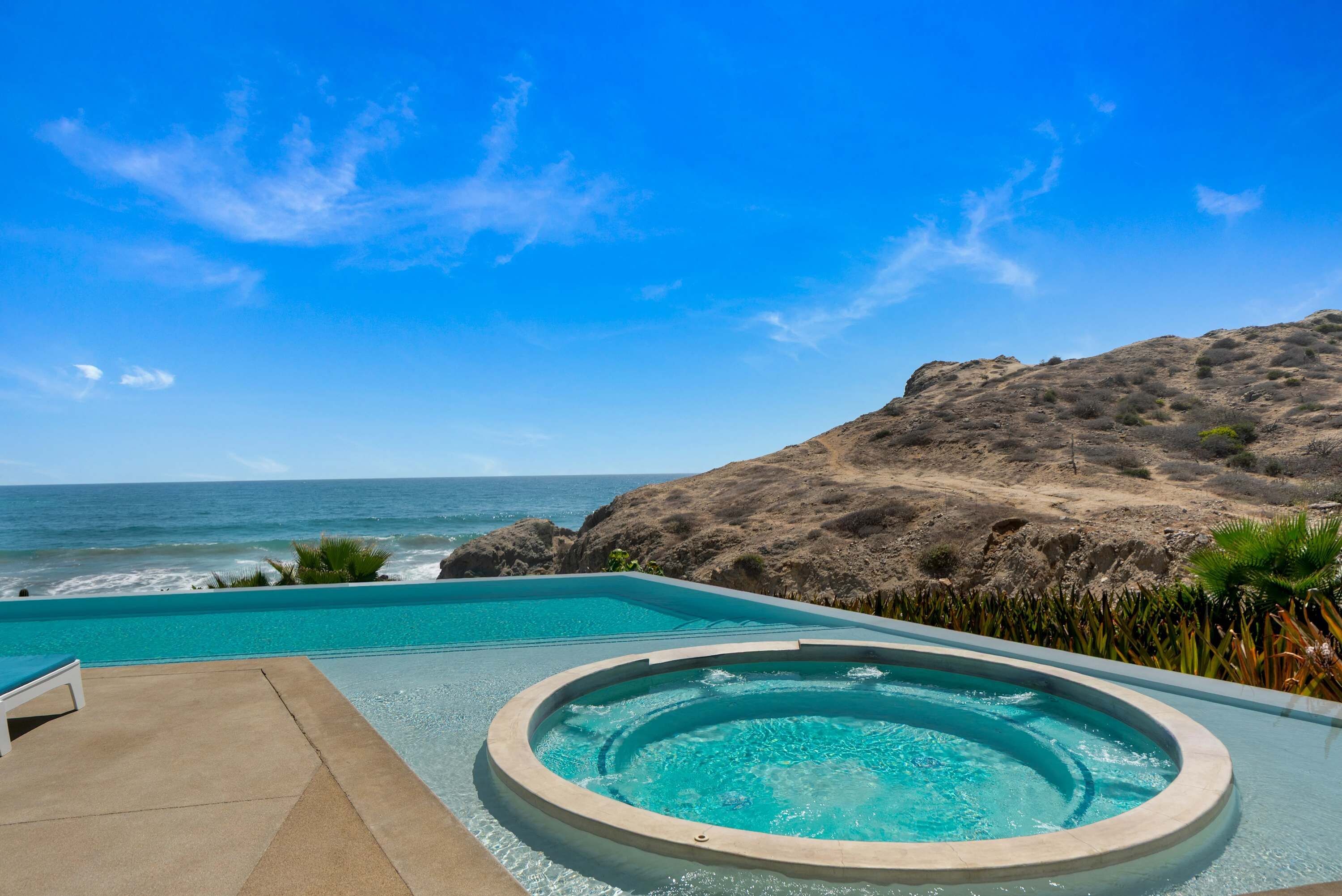 A pool with a view of the ocean and a rocky hillside.
