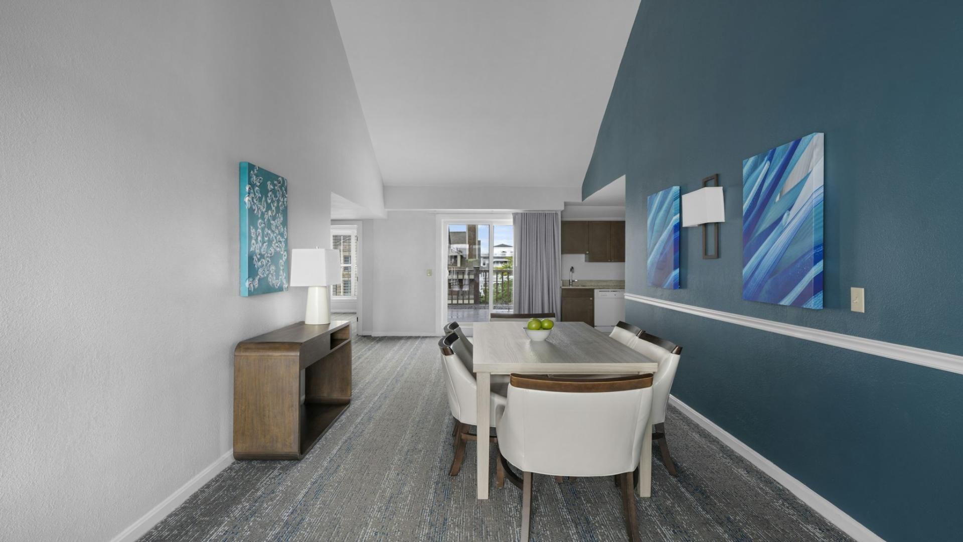 A modern dining area with a table and chairs, a small side table with a lamp, and abstract wall art.