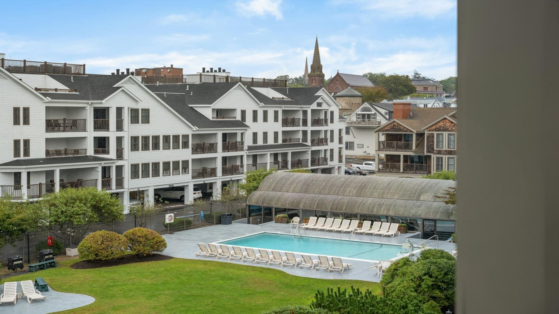 A hotel with a swimming pool, multiple balconies, and a church spire in the background.