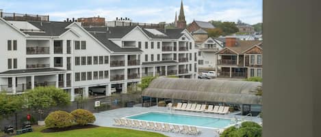 Ett hotell med en swimmingpool, flera balkonger och en kyrktorn som syns i bakgrunden.