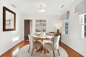 A dining area with a round table, four chairs, a mirror, and shelves with decorative items. - Quaint Cottage-Great Location with Hot Tub! (Mount Pleasant)