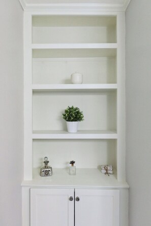 A white shelving unit with multiple shelves, a potted plant, and decorative items. - Quaint Cottage-Great Location with Hot Tub! (Mount Pleasant)