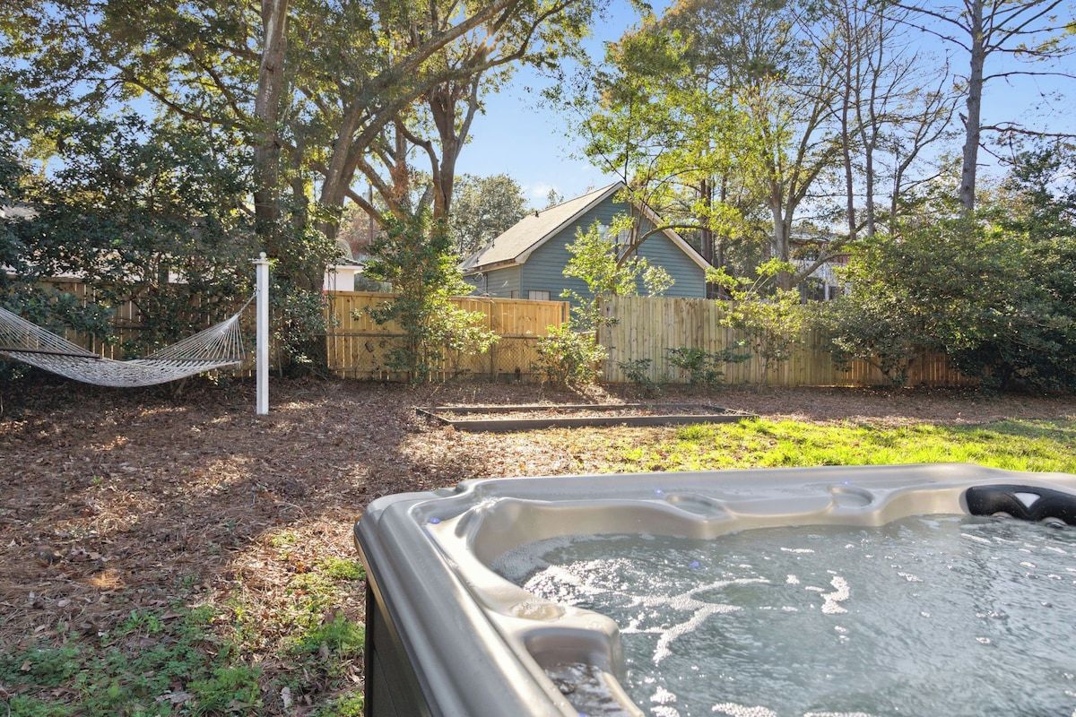 A hot tub in a backyard with a hammock, wooden fence, and trees.