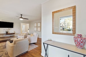 A modern living room with a flat-screen TV, a ceiling fan, and a large mirror above a kitchen counter. - Quaint Cottage-Great Location with Hot Tub! (Mount Pleasant)