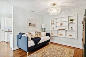 A modern living room with a sofa, a patterned rug, a wall-mounted shelf with decorative items, and a pendant light. - Quaint Cottage-Great Location with Hot Tub! (Mount Pleasant)