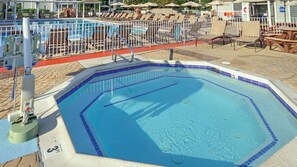 Une piscine dont le bord est revêtu de carrelage, entourée de chaises longues et de parasols.