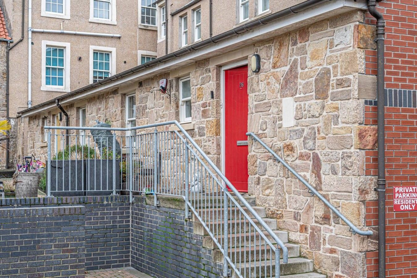 Un edificio de piedra con una puerta roja, una escalera metálica y un letrero que indica estacionamiento privado para residentes.