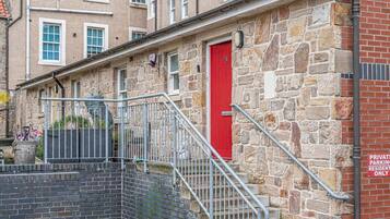 Un edificio de piedra con una puerta roja, una escalera metálica y un letrero que indica estacionamiento privado para residentes.