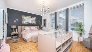 Une chambre à coucher moderne avec un grand lit, des tables de chevet, une coiffeuse et un lustre.
