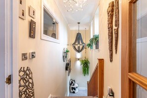 Un pasillo con una araña, luces empotradas en la pared y plantas decorativas.