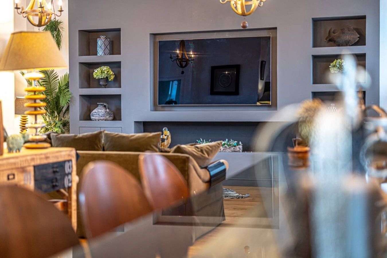 A modern living room with a flat-screen TV mounted on the wall, a sofa with cushions, and decorative items on shelves.