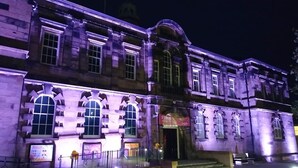 Un bâtiment historique doté d’arcatures et d’une entrée imposante, illuminé la nuit.