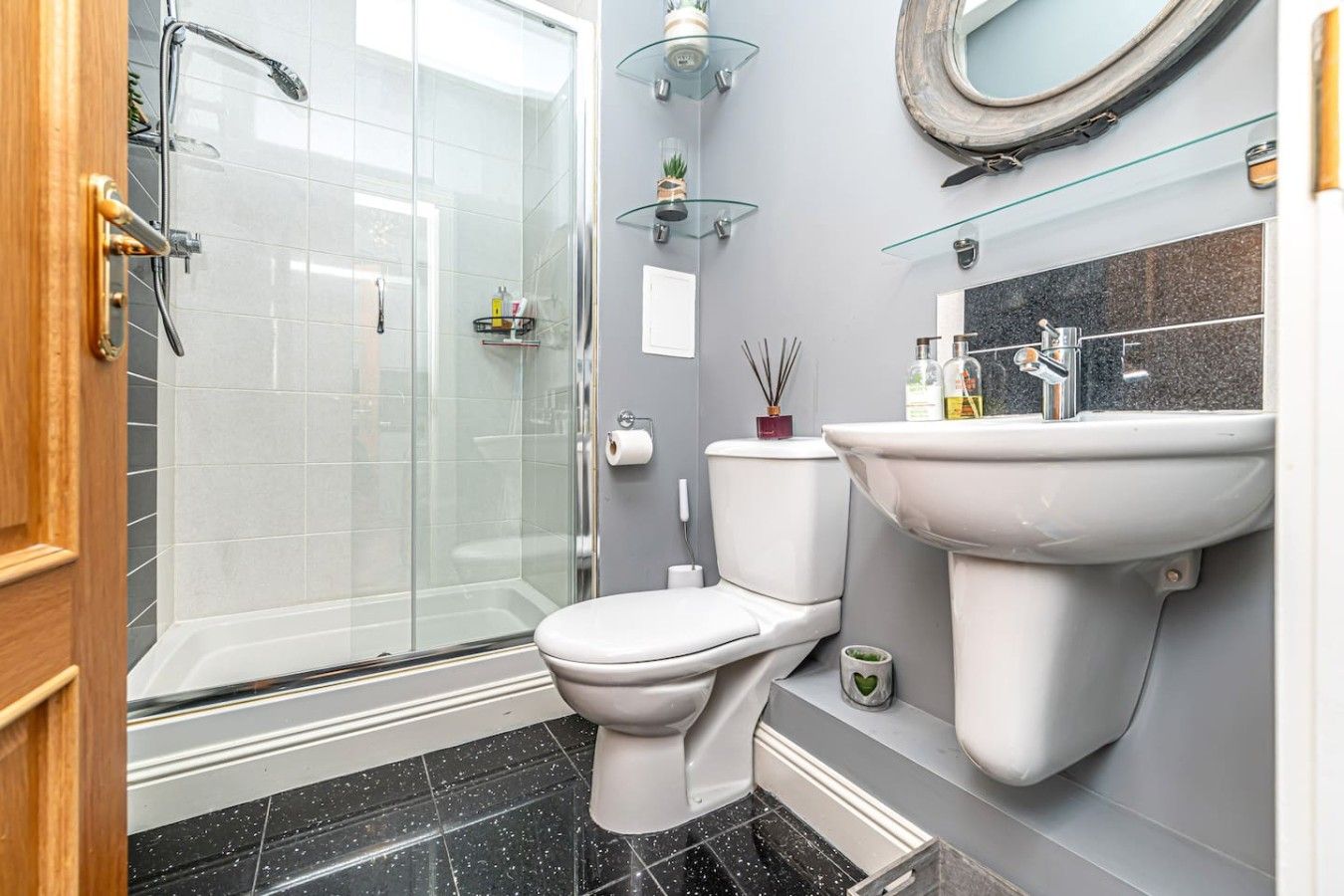 A bathroom with a glass shower enclosure, a toilet, a sink, and a mirror.