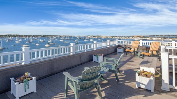 A deck with Adirondack chairs and planters, overlooking a marina with numerous boats.