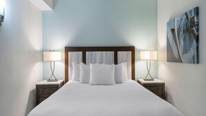 Quarto de hotel com uma cama grande, duas mesas de cabeceira com luminárias, uma cabeceira de madeira e um quadro na parede.