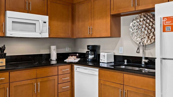 Una cocina con armarios de madera, microondas, cafetera, tostadora y refrigerador.