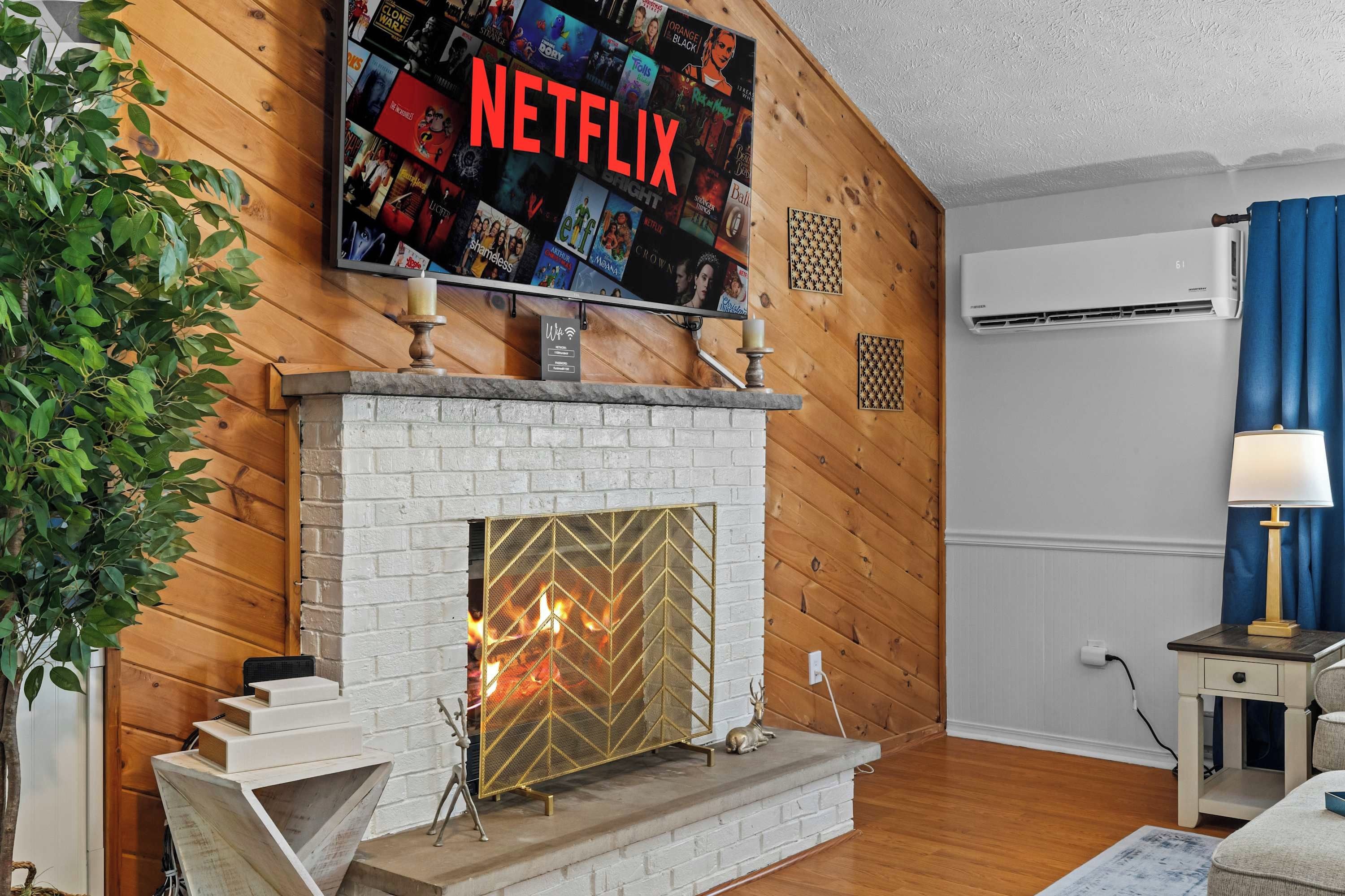 Ein Wohnzimmer mit Kamin, einem an der Wand befestigten Fernseher, der eine Netflix-Oberfläche zeigt, und einer Wand-Klimaanlage.