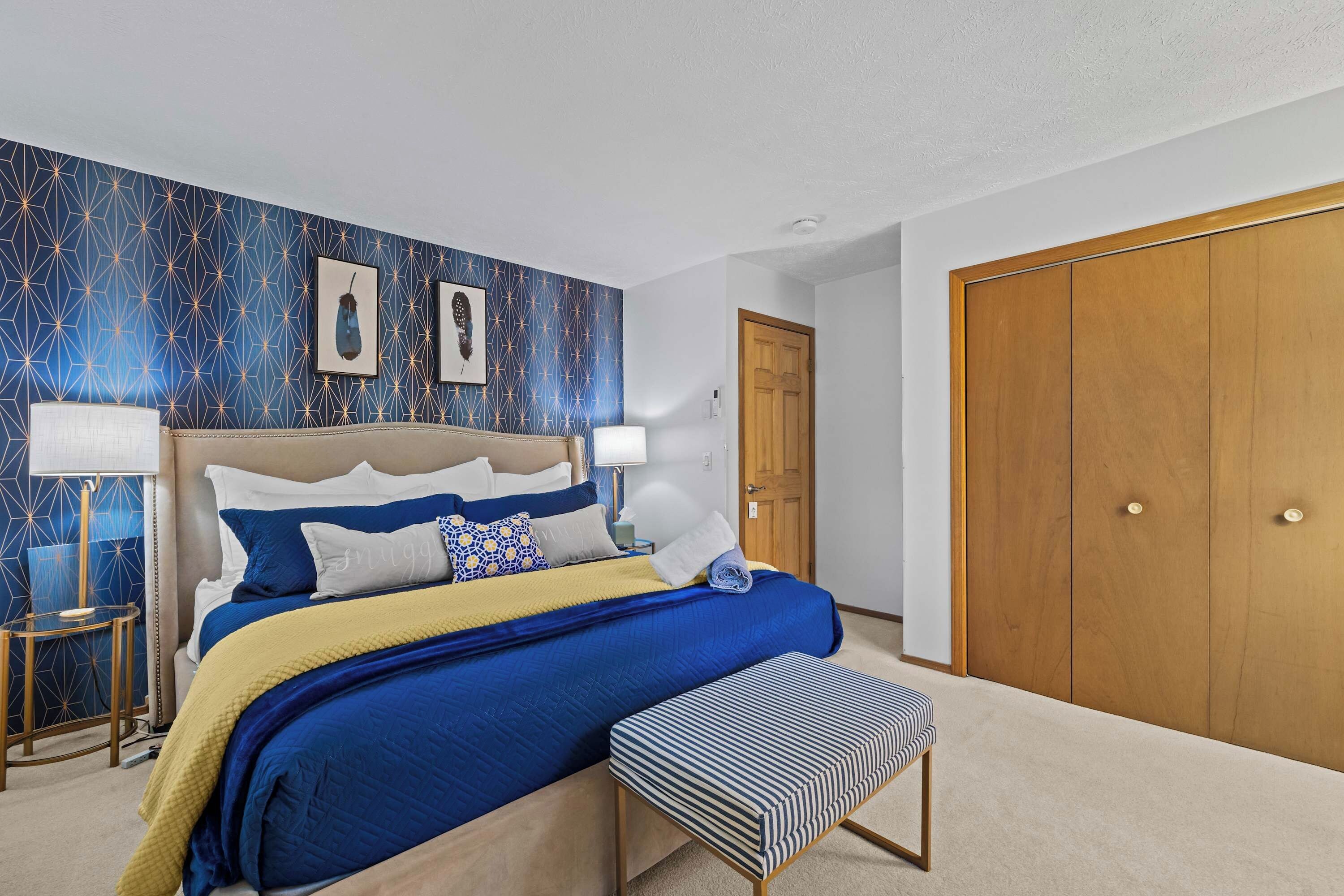 A bedroom with a large bed, bedside tables, a bench, a wardrobe, and a door.