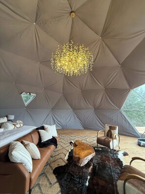 A tented accommodation with a central chandelier, leather seating, and a wooden coffee table.