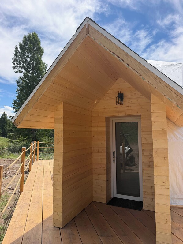 A wooden cabin with a sloped roof, a glass door, and a wooden deck.