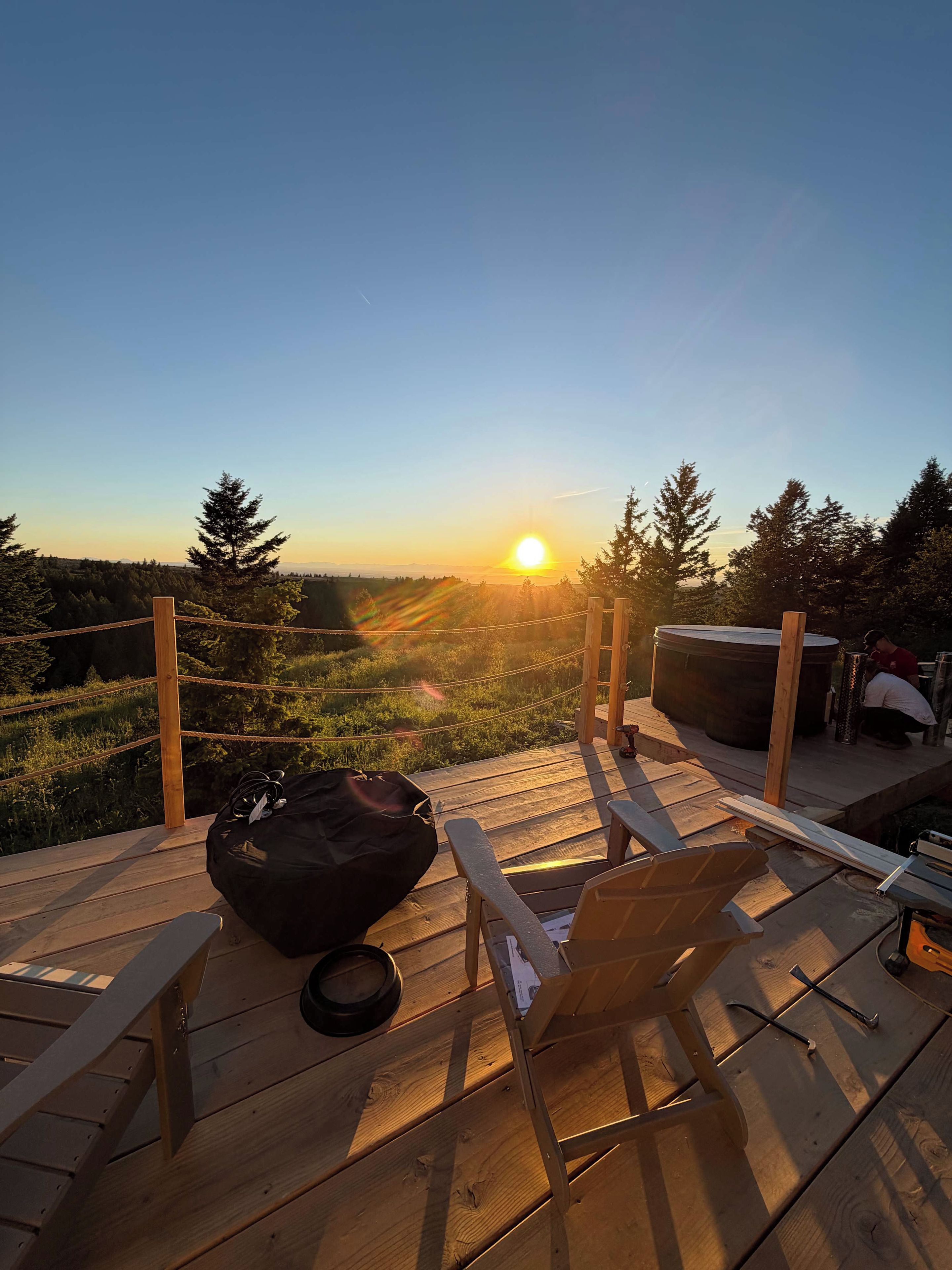 A wooden deck with a view of the sunset, a black bean bag, and a metal grill.