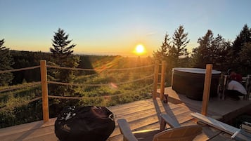 A wooden deck with a view of the sunset, a black bean bag, and a metal grill.