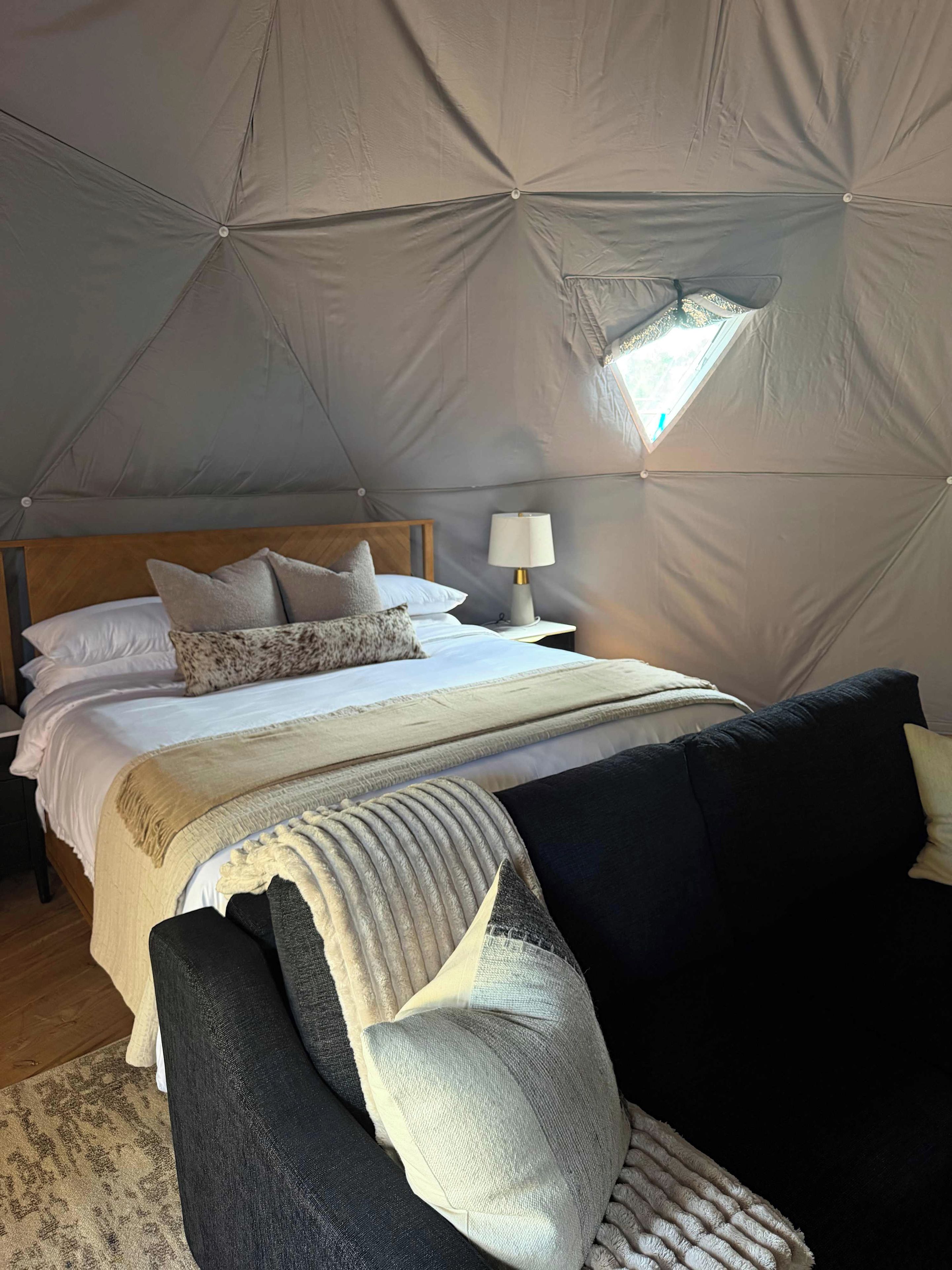 A tent-style bedroom with a bed, pillows, a bedside lamp, and a view of the outdoors.