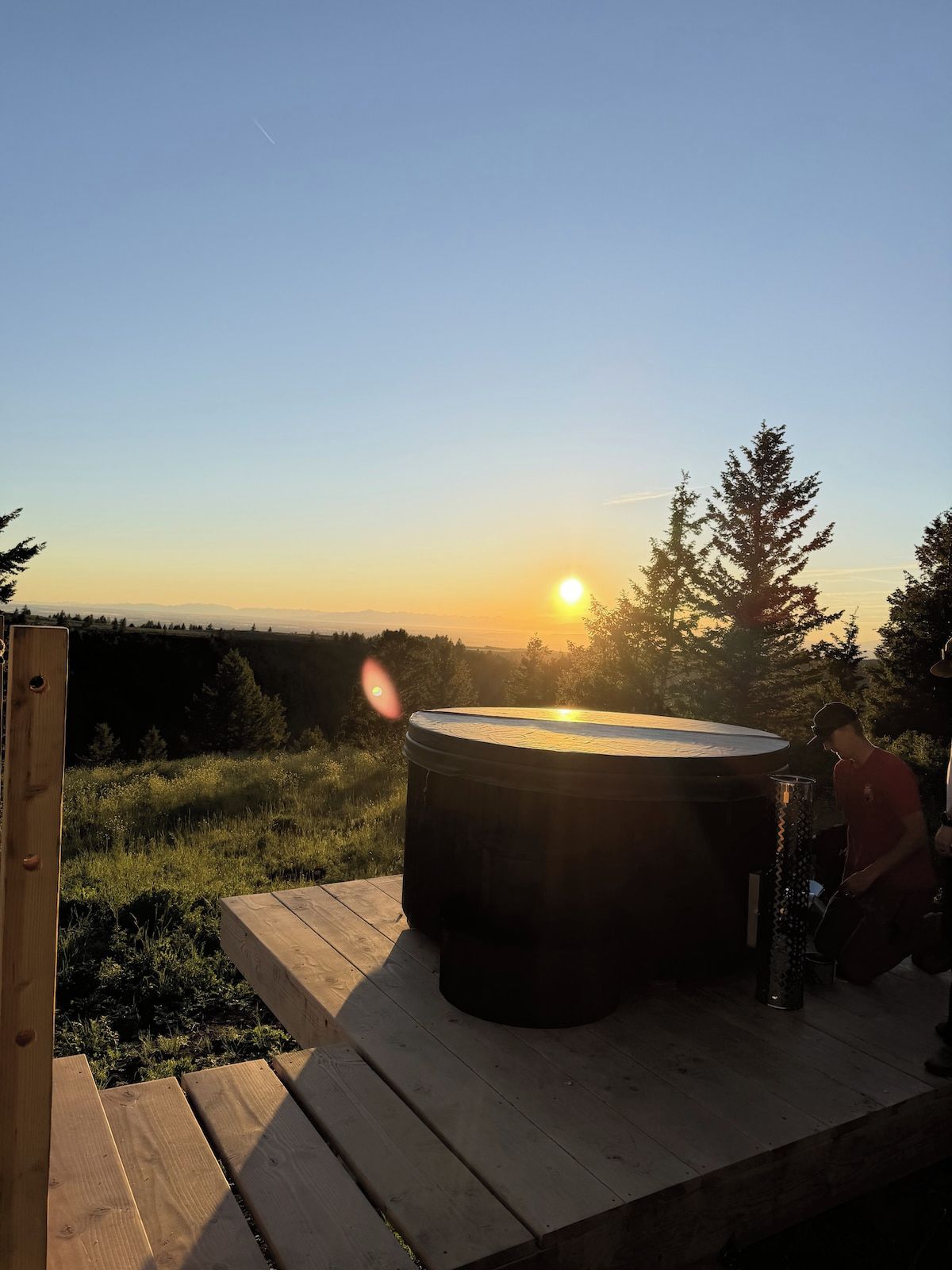 Boblebad på træterrasse med udsigt til solnedgang og træer i baggrunden.