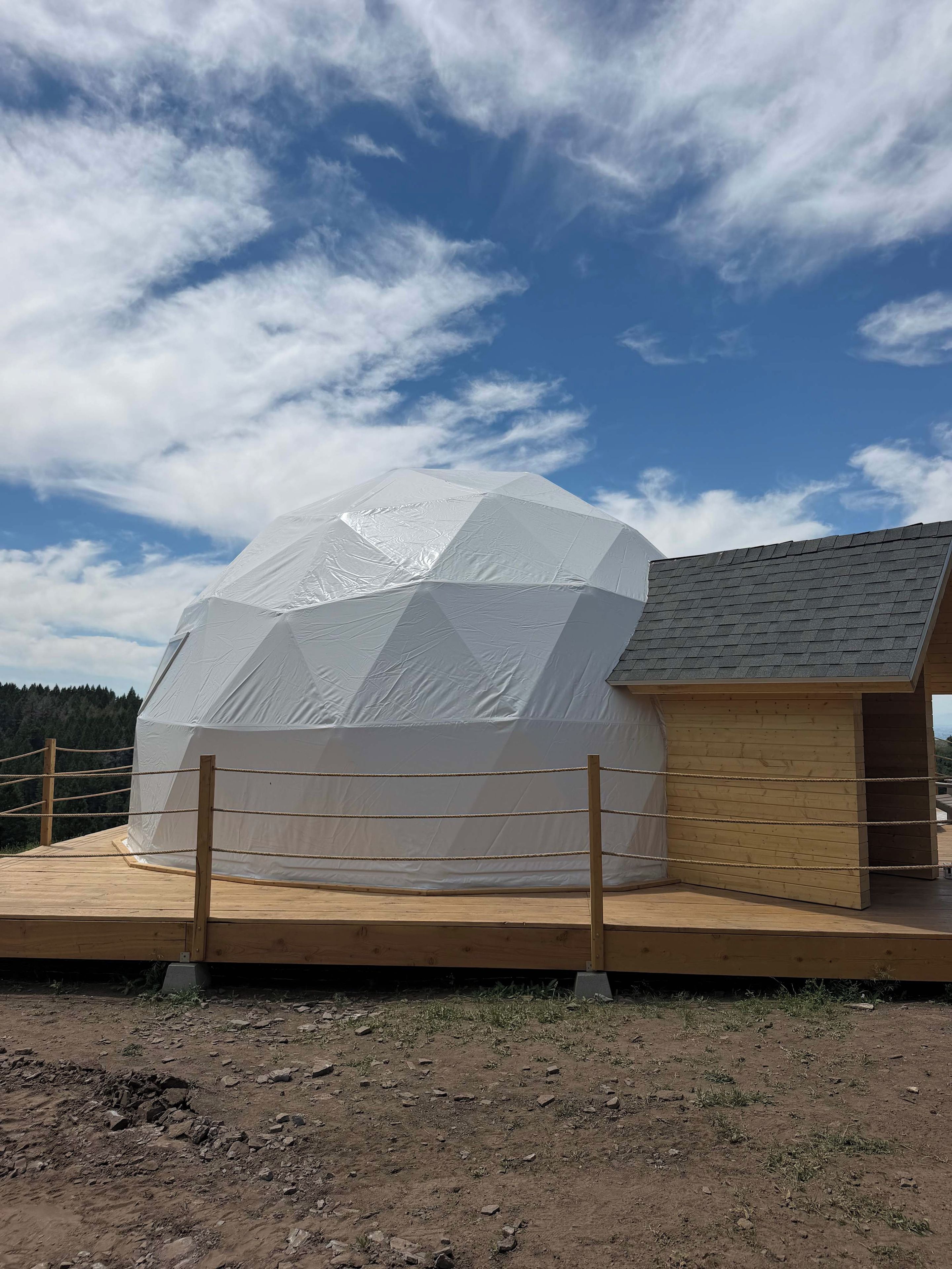 A geodesic dome structure with a wooden deck and a small building with a sloped roof.