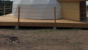 Uma estrutura em cúpula geodésica com um deck de madeira e um pequeno edifício com telhado inclinado.