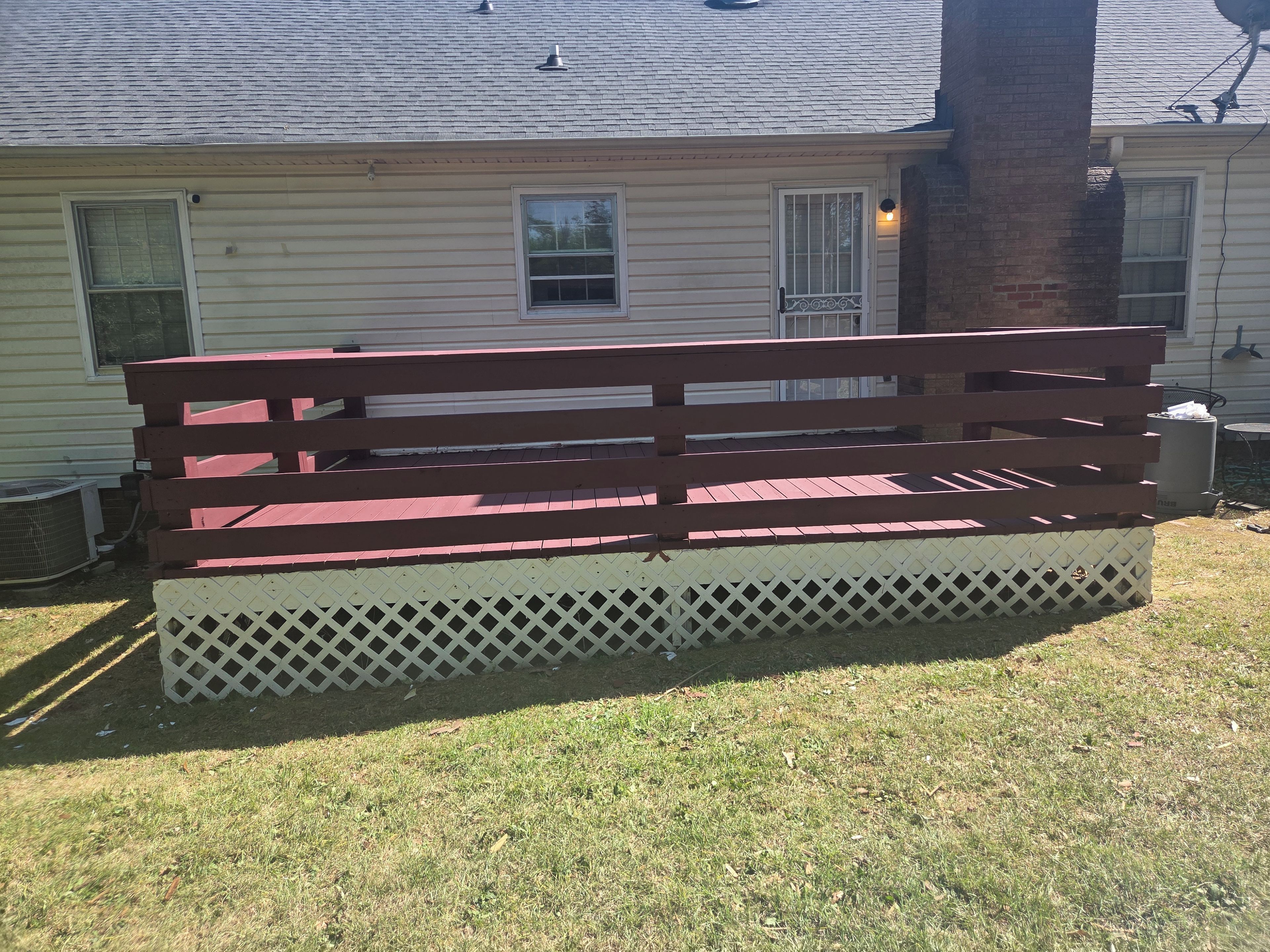 Un banc en bois doté d’une base ajourée, placé devant une maison ornée d’un pilier en briques et d’une fenêtre avec une grille en métal.