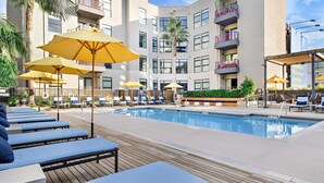 A pool area with lounge chairs and umbrellas, surrounded by a multi-story building with balconies. - Botanical Escape' Large Balcony Heart of Hollywood (Los Angeles)