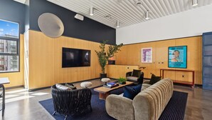 A modern lobby with a sofa, chairs, a coffee table, a TV, a fan, a plant, and a poster. - Botanical Escape' Large Balcony Heart of Hollywood (Los Angeles)
