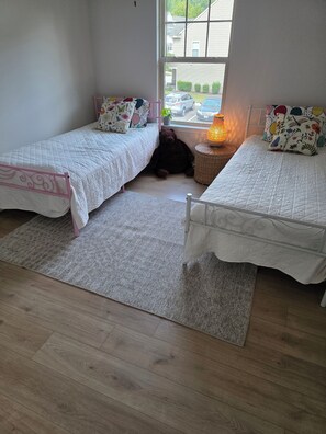 A bedroom with two single beds, a window, a lamp, and a teddy bear.