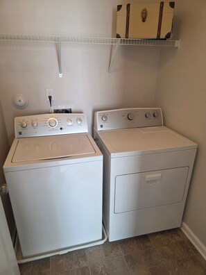 A laundry room with two white washing machines and a shelf above.